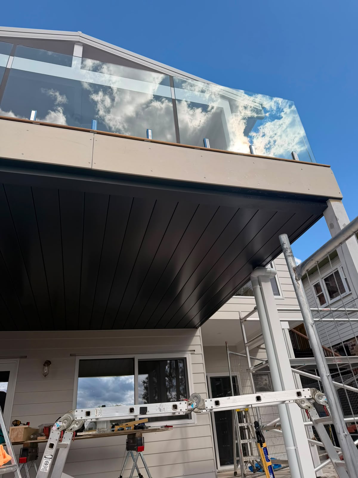 Underdeck ceiling with dark linear soffit lining and frameless glass balustrade above