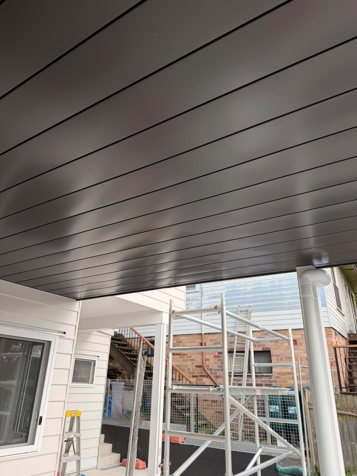 Underdeck soffit lining with glass balustrade visible above and scaffolding on site