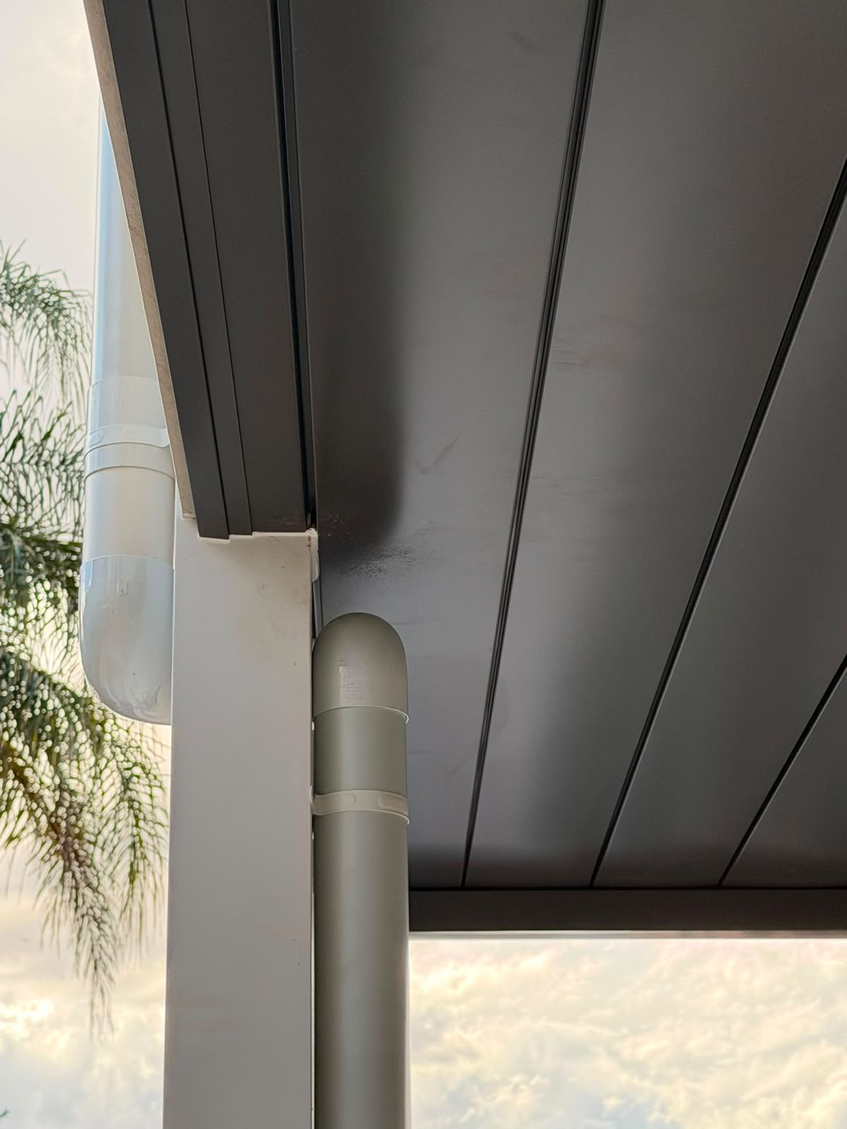 Patio corner with downpipe and gutter outlet against dark soffit lining